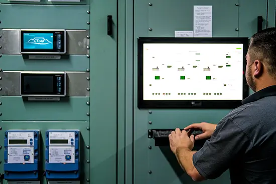Man typing on an input device in a power control room with plant equipment in green steel casing